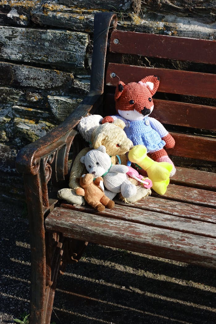 A collection of stuffed toy animals arranged on an old wooden bench outdoors.